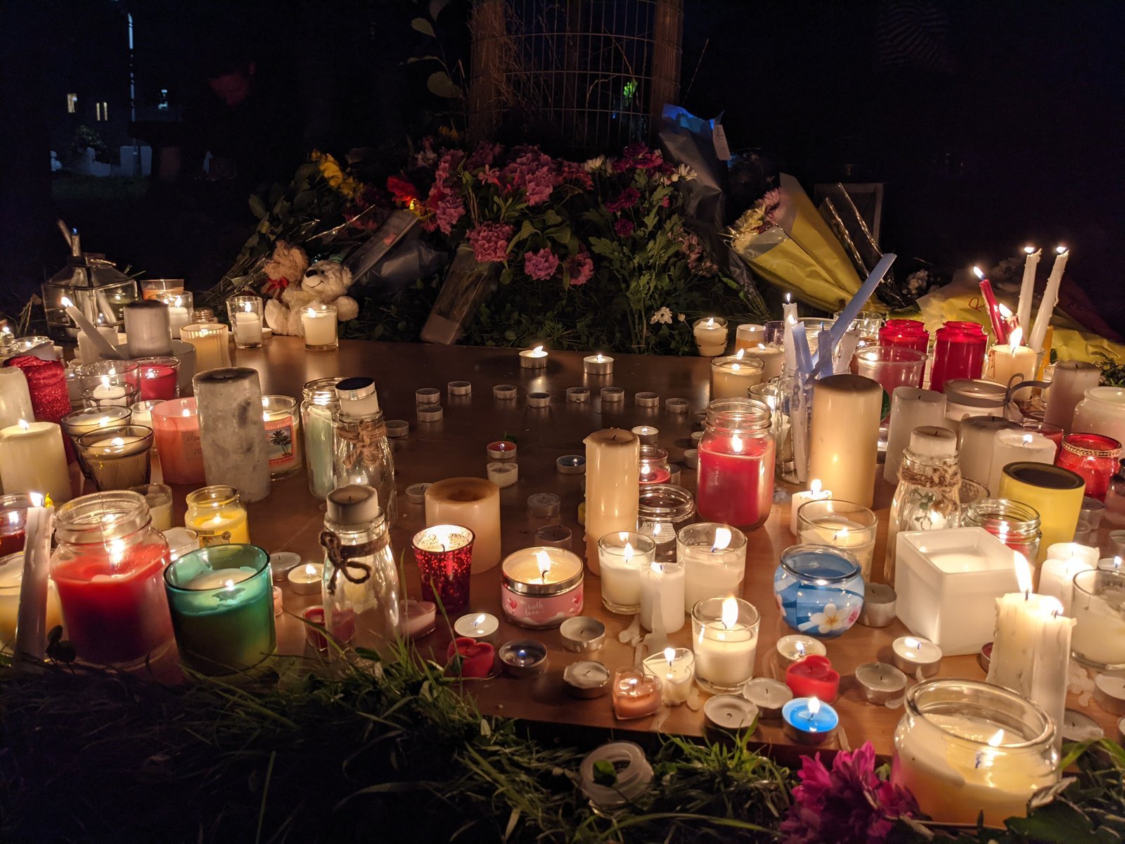 A memorial of flowers and candles outside a home.